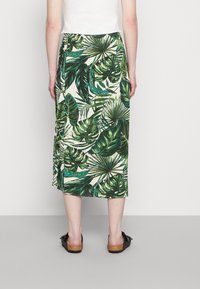 Jupe midi à motif floral présentant un imprimé de feuilles tropicales vertes vives sur un fond clair, fabriquée en tissu léger avec une coupe décontractée.