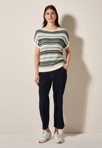 Randig stickad tröja i grönt, krämfärgat och rosa med en avslappnad passform, ribbad halsringning och korta ärmar, matchad med mörka denimbyxor och vita sneakers.