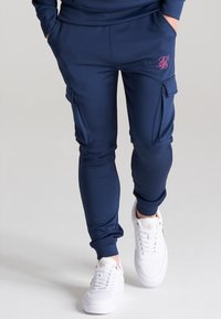 Marina cargo joggers i ett slätt material, med sidofickor och åtsittande muddar, tillsammans med vita sneakers med gyllene detaljer.