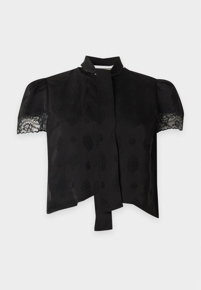 Blouse noire à manches courtes avec manches bouffantes bordées de dentelle, tissu à motif subtil et détail de lien étroit au col.