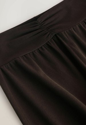 Dunkelbrauner Jersey-Rock mit einem gerafften Bund und weicher Textur, der fließenden Stoff hat, der nach unten fällt.