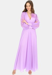 Długa, zwiewna lawendowa sukienka z przezroczystymi długimi rękawami, dekoltem w serek i piórami na ramieniu. Wykonana z lekkiego materiału.