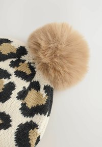 Pletená čepice s leopardím vzorem v černé a béžové barvě, zakončená měkkou, nadýchanou béžovou pom-pom kouli. Textura je útulná a teplá.