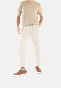 T-shirt beige à manches courtes, pantalon crème ajust�é et chaussures en daim marron. L'ensemble est agrémenté d'une ceinture tissée et d'une coupe décontractée.