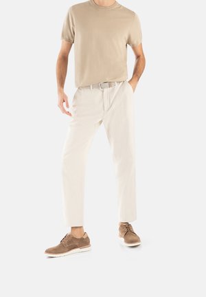 Beige T-Shirt mit kurzen Ärmeln, cremefarbene, schmal geschnittene Hose und braune Wildlederschuhe. Das Outfit verfügt über einen geflochtenen Gürtel und einen lässigen Schnitt.
