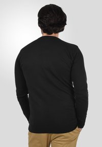 Sort bomuldsweater med lange ærmer, ribbede manchetter og kant. Tæt siddende design, set fra ryggen, parret med khaki bukser.