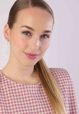 Hellrosa Vichy-Kleid mit rundem Ausschnitt, kombiniert mit silbernen, herzförmigen Ohrringen. Glattes Haar, zu einem Ponytail frisiert.