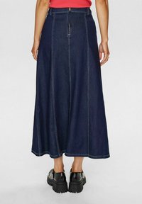 Tumši džinsas maxi svārki ar redzamām šuvēm, ar rāvējslēdzēju un plūstošu siluetu. Apvienoti ar spīdīgām melnām platformatām kurpēm.