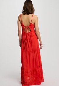 Red maxi dress with a tiered design, back cutout, and adjustable tie closure. Fabric features embroidered floral details at the hem.