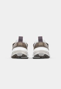 Tossut, joissa on valkoinen ja ruskea päällinen, verkkomateriaali ja pehmustetut nilkkareunat. Päällä on selkeä pohja, jossa on tekstuurilla varustettu kumipohja.