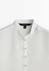 Chemise blanche à col mandarin avec patte de boutonnage cachée et quatre boutons visibles, étiquette Massimo Dutti, taille XS.