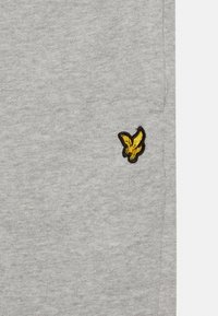 Szara bluza z miękką teksturą, ściągaczami przy mankietach oraz żółtym haftowanym logo orła po lewej stronie klatki piersiowej.