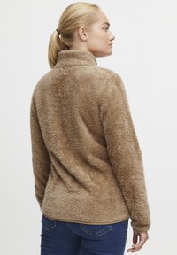 Brown fleece jacket with a high collar, soft texture, side zip, and casual fit, featuring a smooth finish and back seam detailing.