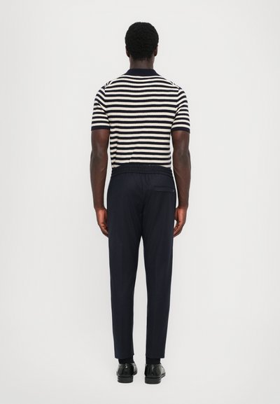 Suéter de manga corta a rayas en marino y crema, combinado con pantalones marinos oscuros que cuentan con una cintura elástica. Calzado negro completa el look.