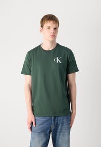 Grøn bomulds t-shirt med rund halsudskæring og korte ærmer. Har et hvidt "cK" logo på venstre bryst. Klassisk afslappet pasform.