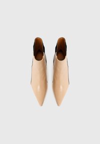 Bottines en cuir beige à bout pointu, avec des accents latéraux noirs et une finition lisse et brillante. Présente un petit talon et un design ouverte à l'arrière.