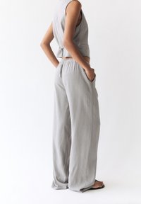Haut sans manches gris et pantalon large en tissu léger. Le pantalon présente une taille élastique et des poches sur les côtés.