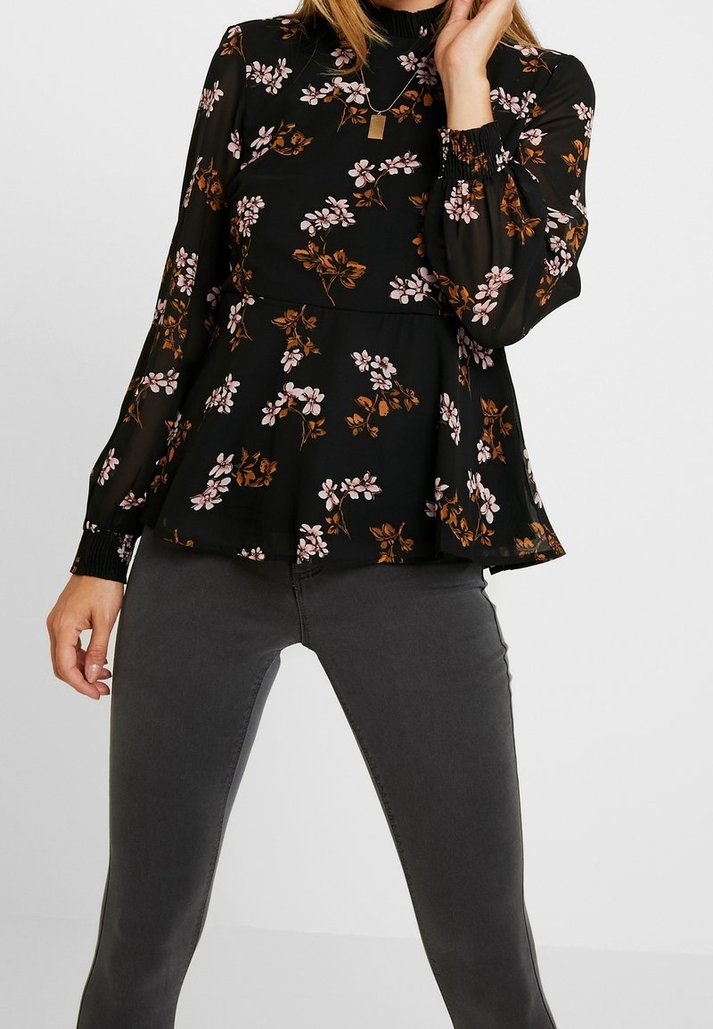Schwarze Bluse mit langen Ärmeln, die mit pinken und braunen Blumenmustern verziert ist, mit Rüschensaum an Kragen und Ärmeln sowie einem Peplum-Taille-Design.