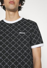 Black short-sleeve t-shirt with white geometric pattern, contrast white collar, and a small "ellesse" label on the chest. Cotton fabric.