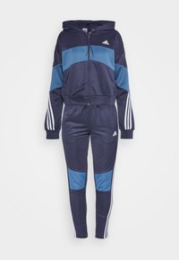 Survêtement Adidas bleu marine et bleu clair avec sweat à capuche zippé et pantalon assorti comportant des bandes blanches sur les manches et les jambes.