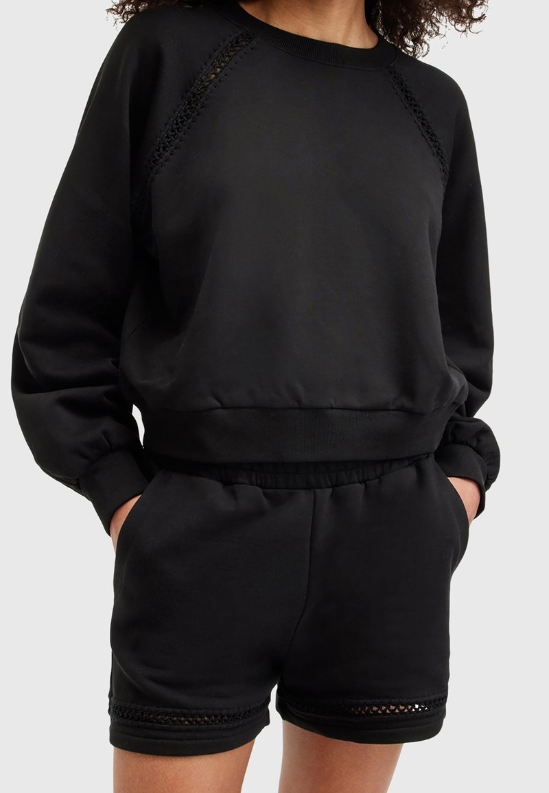 Czarna bluza z teksturowanymi raglanowymi rękawami i prążkowanym dołem, zestawiona z dopasowanymi szortami z koronkowym detalem na dole.