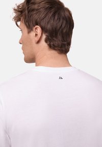 Weißes Baumwoll-T-Shirt mit einem schlichten Design, kurzen Ärmeln und einem kleinen schwarzen Logo auf der Rückseite nahe dem Ausschnitt.