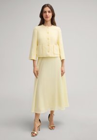 Completo in due pezzi composto da una giacca gialla corta e testurizzata con quattro bottoni e tasche, e una gonna gialla fluida coordinata.