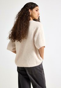 Uldent beige striktrøje med korte ærmer, afslappet pasform og rundet kant. Bruges med mørkegrå bukser med lommer og afslappet stil.