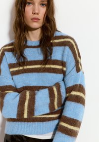 Pulover în dungi, de culoare bleu deschis, maro și galben. Textură moale și pufoasă, cu dungi orizontale largi. Guler rotund și croială lejeră.