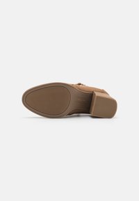 Chaussure à talons marron avec un embout carré et un talon bloc. Tige en matériau lisse avec une semelle en caoutchouc texturé et un détail de fermeture éclair sur le côté.
