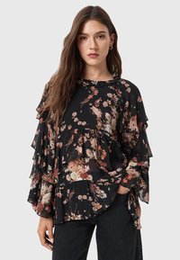 Blusa nera floreale con rouches a strati, realizzata in tessuto leggero. Presenta un colletto rotondo e vari motivi floreali nei colori rosa, arancione e crema.