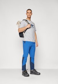 Camiseta gris con el logo de Columbia, pantalones azul y marino de corte ajustado, y zapatos de senderismo negros, que cuentan con materiales duraderos y detalles de costura.