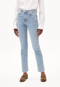 Light blue high-waisted straight-leg jeans with whiskering details, featuring five pockets and a metal button closure. Worn with leopard print flats.