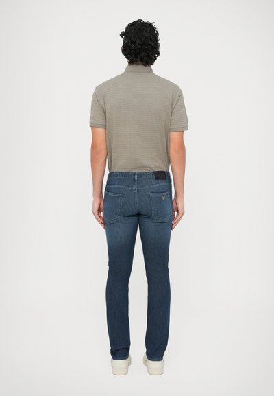 Sivé tričko s krátkym rukávom typu polo a tmavomodré džínsové nohavice. Polo tričko má textúrovaný vzor, nohavice sú priliehavé s zadnými vreckami a čiernou nálepkou.