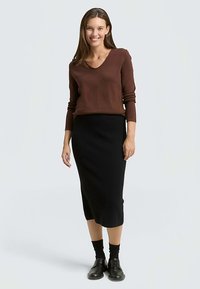 Maglione marrone a scollo a V, gonna midi nera aderente e scarpe nere. L'outfit presenta una texture liscia con un design semplice e classico.