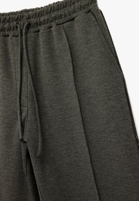 Dunkelgraue Sweatpants mit elastischem Bund, Kordelzug, Seitentaschen und kontrastierenden Reißverschlüssen entlang der Beine. Weicher Stoff.
