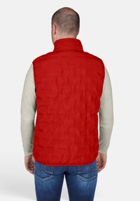 Rote gesteppte Weste mit hohem Kragen, mit glatter Außenseite, getragen über einem hellgrauen Langarmshirt und blauen Jeans.