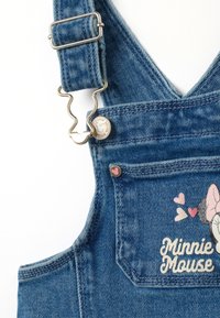 Jeanslatzhosen mit verstellbaren Trägern, einem Metallverschluss und einer Fronttasche mit einem Minnie-Maus-Graphic und Herzakzenten. Blaue Farbgebung.