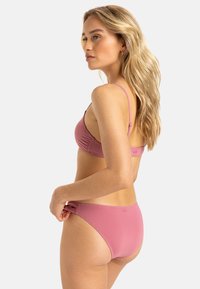 Růžový bikiny set s nahrnutou texturou na vršku a hladkým spodním dílem. Popruhový design s nastavitelnými pásky, minimalistický styl a bezšvové provedení.