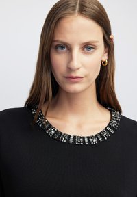 Suéter negro con cuello de cuentas con adornos plateados y transparentes, escote redondo y textura acanalada.