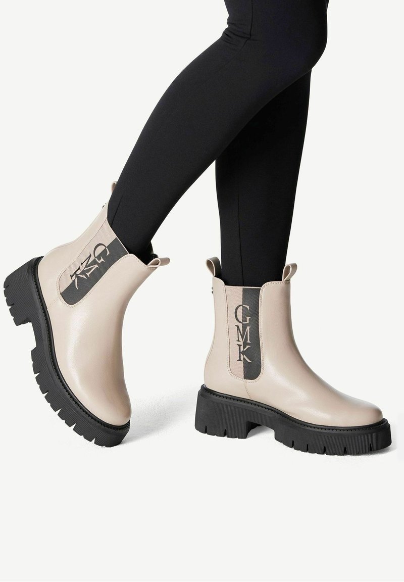 Bottines beiges en cuir avec semelles épaisses noires et logo GMK sur les côtés élastiques portées avec des leggings noirs.