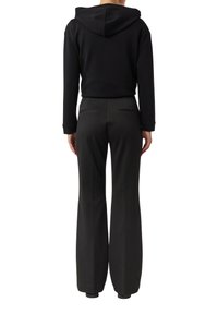 Czarna bluza z kapturem o luźnym kroju, zestawiona z eleganckimi czarnymi spodniami dzwonami, posiadającymi tylne kieszenie i gładką fakturę.