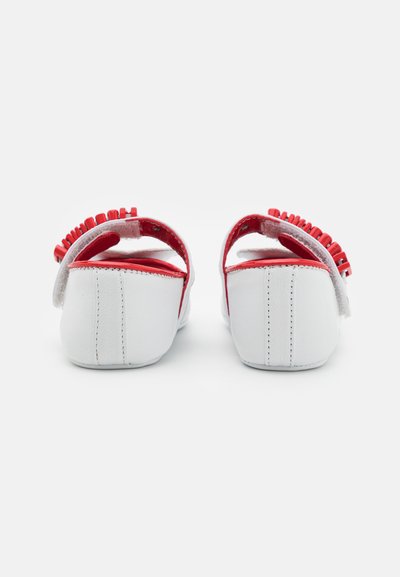 White sandals with red accents, featuring a curved shape and a textured upper with small loops. Soft material with an adjustable strap.