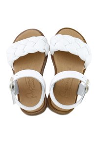 Par de sandalias blancas con tiras delanteras entrelazadas, tiras de tobillo con hebillas y plantillas acolchadas de color marrón claro sobre un fondo blanco.