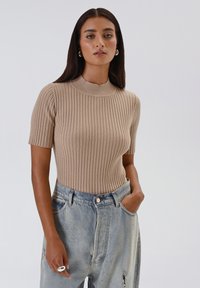 Top beige a righe a maniche corte con colletto alto, realizzato in un materiale a maglia testurizzato, abbinato a jeans in denim blu chiaro a vita alta.