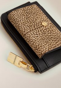 Portafoglio in pelle nera con una patta in tessuto marrone dorato. Presenta una zip e un fermo in oro, con cuciture visibili lungo i bordi.