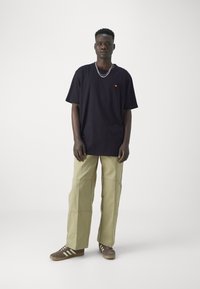 Schwarzes Baumwoll-T-Shirt mit kleinem orangefarbenen Logo, kombiniert mit beigen weit geschnittenen Cargo-Hosen und braunen Sneakers mit weißen Streifen.