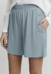 Ljusblå shorts med elastiskt midjeband, avslappnad passform och sidofickor. Tillverkade av ett mjukt material med subtil lyster och utan synliga mönster.