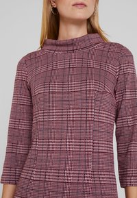 Maroon ja valge ruuduline kleit kõrge kaelusega ja kolmeveerandiga varrukatega. Omab tekstuurilist kangast, millel on peen houndstooth mustr.