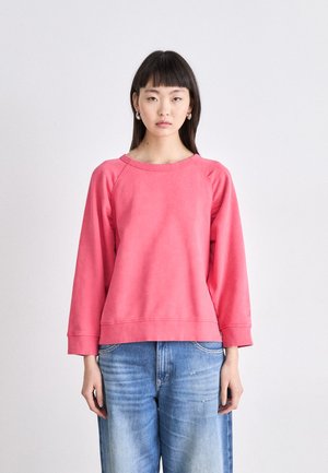 Light pink sweatshirt with a relaxed fit, raglan sleeves, rounded neckline, and ribbed cuffs, paired with denim jeans.